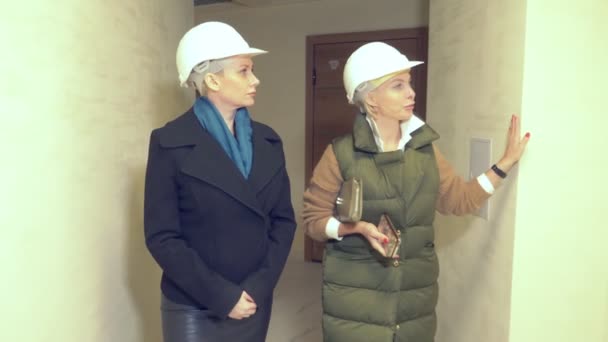 Dos mujeres con cascos blancos. hablar dentro de un edificio en construcción — Vídeo de stock