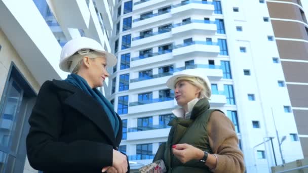 Twee vrouwen in witte helmen praten op de achtergrond van het gebouw — Stockvideo