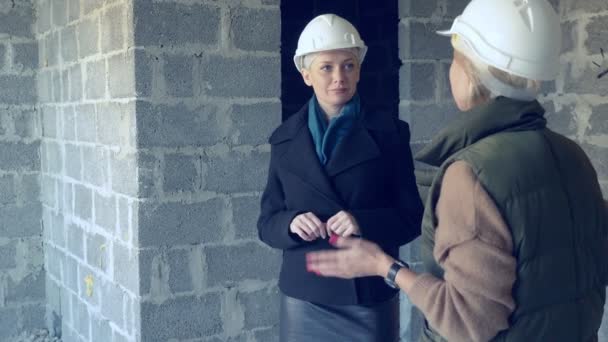 Zwei Frauen in weißen Helmen sprechen drinnen mit grobem Schnitt — Stockvideo