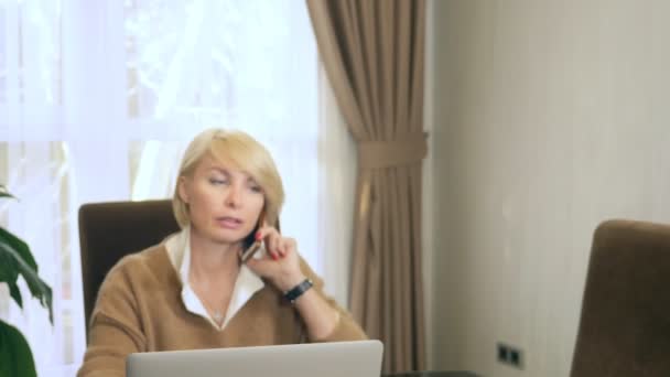 Kvinna på kontoret pratar i telefon tittar på laptop — Stockvideo