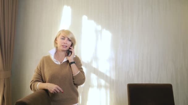 Hermosa mujer hablando en un teléfono celular, de pie en la oficina junto a la ventana — Vídeo de stock