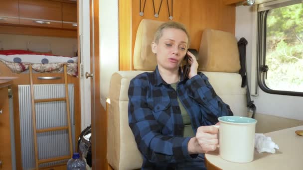 Женщина использует мобильный телефон, сидя за столом в доме на колёсах — стоковое видео