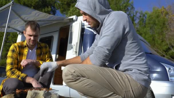 Twee mannen koken vlees op de grill bij de campers in de natuur — Stockvideo