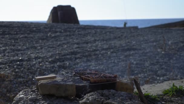Cooking meat grilled on a makeshift grill out of rocks by the sea — Stock Video
