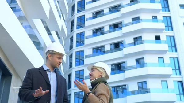 Ein Mann und eine Frau in weißen Helmen unterhalten sich auf dem Hintergrund eines Gebäudes — Stockfoto