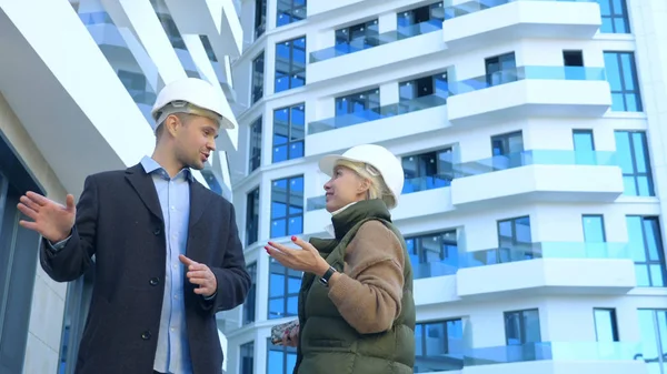 Ein Mann und eine Frau in weißen Helmen unterhalten sich auf dem Hintergrund eines Gebäudes — Stockfoto