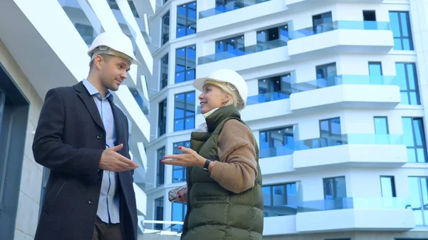 Ein Mann und eine Frau in weißen Helmen unterhalten sich auf dem Hintergrund eines Gebäudes — Stockfoto