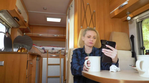 Woman uses a cell phone while sitting at a table in a motorhome — Stock Photo, Image