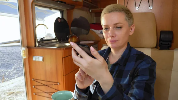 Женщина использует мобильный телефон, сидя за столом в доме на колёсах — стоковое фото