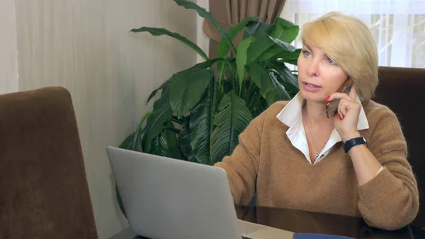 Femme au bureau parlant au téléphone regardant un ordinateur portable — Photo