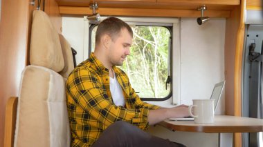 Adam laptopunu kullanarak karavanda bir masada oturuyor.