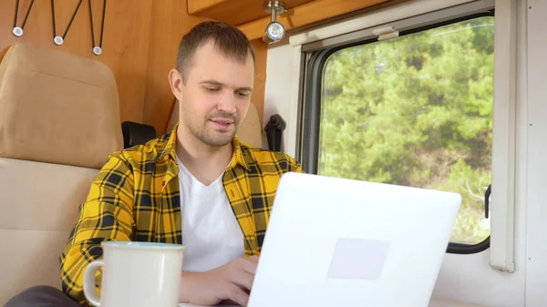 Uomo che usa il suo computer portatile seduto a un tavolo nel camper — Foto Stock