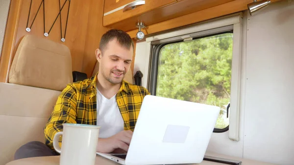 Homme utilisant son ordinateur portable assis à une table dans le camping-car — Photo