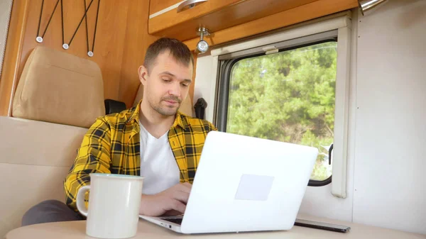 Homme utilisant son ordinateur portable assis à une table dans le camping-car — Photo