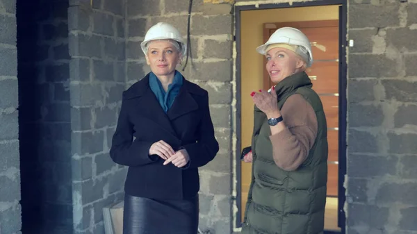 Due donne in caschi bianchi che parlano al chiuso con finiture ruvide — Foto Stock