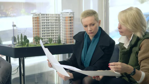 Deux femmes parlent, assises dans le bureau de vente sur le fond de la disposition du bâtiment — Photo