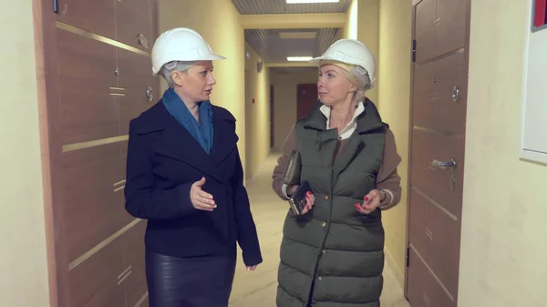 Dos mujeres en cascos blancos hablando en interiores con borde áspero — Foto de Stock