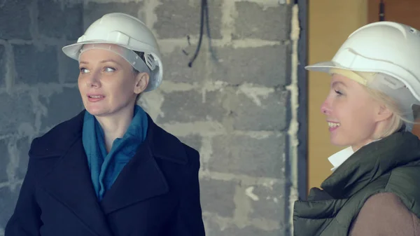 Duas mulheres em capacetes brancos falando dentro de casa com guarnição áspera — Fotografia de Stock
