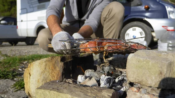 Un hombre cocina carne en la parrilla al aire libre sobre un fondo de autocaravanas —  Fotos de Stock
