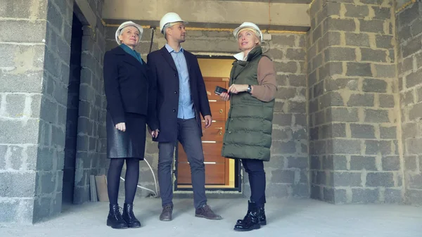 Deux femmes et un homme en casque blanc. parler sur le fond du bâtiment — Photo