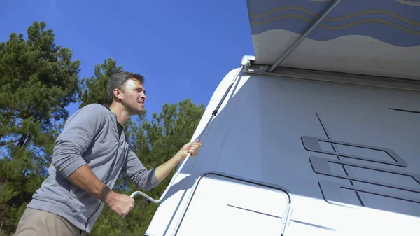 Um homem monta um dossel do sol em uma caravana contra um céu azul claro — Fotografia de Stock