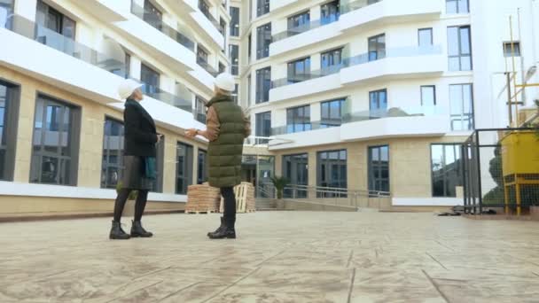 Dos mujeres en cascos blancos están hablando en el fondo del edificio — Vídeos de Stock