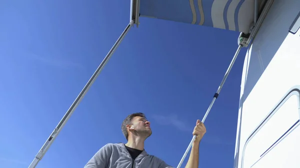 Seorang pria memasang kanopi dari matahari di sebuah rumah bermotor melawan langit biru yang cerah — Stok Foto