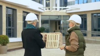 Beyaz kasklı iki kadın binanın arka planında konuşuyor.