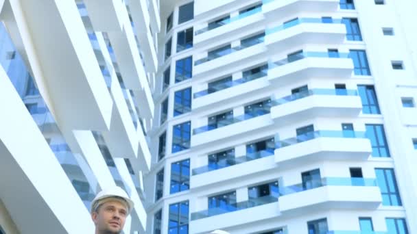 Un hombre y una mujer con cascos blancos están hablando en el fondo de un edificio — Vídeo de stock