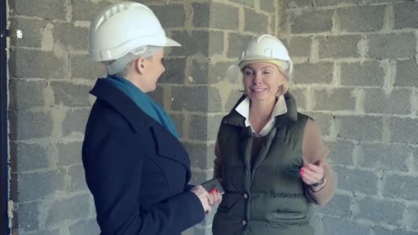 Twee vrouwen in witte helmen praten binnen met ruwe trim — Stockvideo