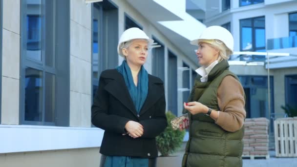 Две женщины в белых шлемах разговаривают на заднем плане здания — стоковое видео