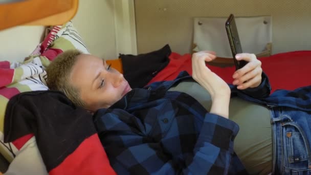 Woman uses a mobile phone lying on a bed in a motor home — Stock Video