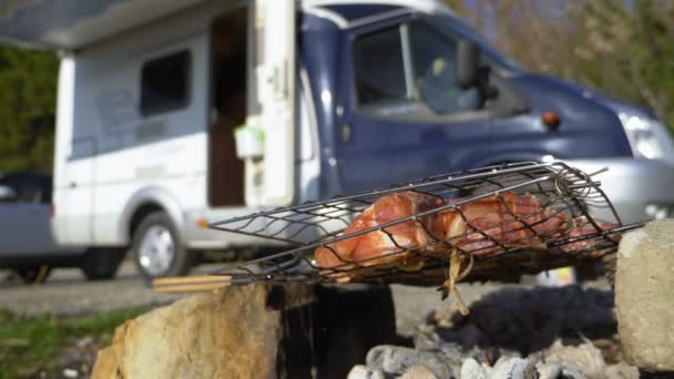 Un hombre cocina carne en la parrilla al aire libre sobre un fondo de autocaravanas — Vídeo de stock