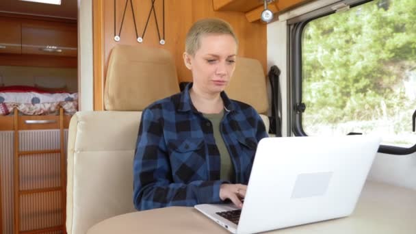 Een vrouw gebruikt een laptop terwijl ze aan een tafel in een camper zit. — Stockvideo