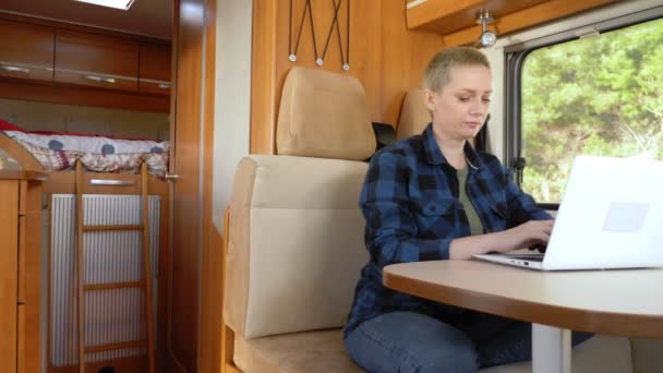 Een vrouw gebruikt een laptop terwijl ze aan een tafel in een camper zit. — Stockvideo