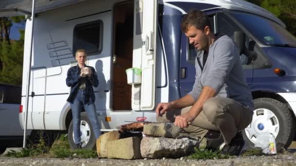 Un hombre cocina carne en la parrilla al aire libre sobre un fondo de autocaravanas — Vídeos de Stock
