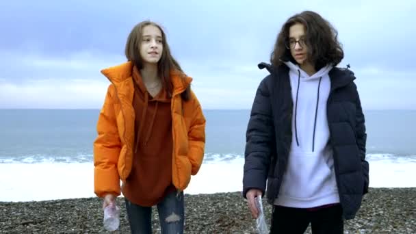 Adolescentes tiran basura de plástico en la playa en el otoño . — Vídeo de stock