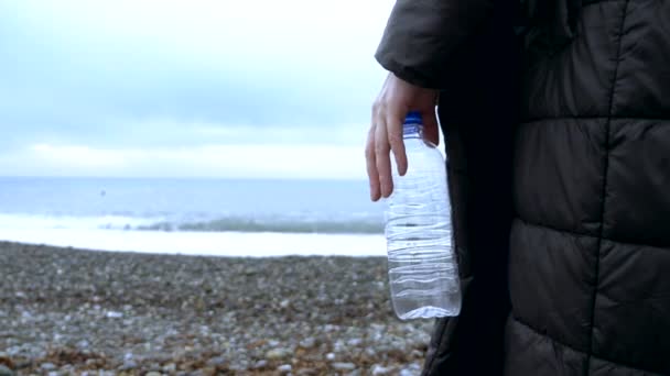 Een close-up. een vrouw gooit een lege plastic fles op het strand. — Stockvideo