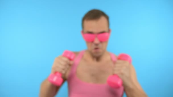 Der verspielte gutaussehende Mann im pinkfarbenen T-Shirt ist mit pinkfarbener Brille und pinkfarbenen Hanteln fit. helle Fitness. Sportmodeaccessoires — Stockvideo