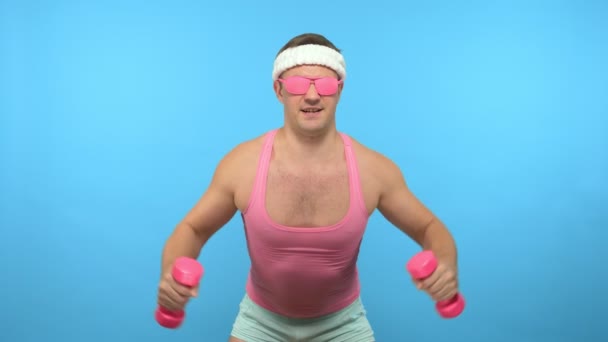 Hombre guapo juguetón en una camiseta rosa se dedica a la aptitud en gafas de color rosa con mancuernas de color rosa. Bright Fitness. Accesorios de moda deportiva — Vídeos de Stock