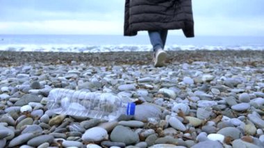 Yakın plan. Bir kadın kumsala boş bir plastik şişe atıyor..
