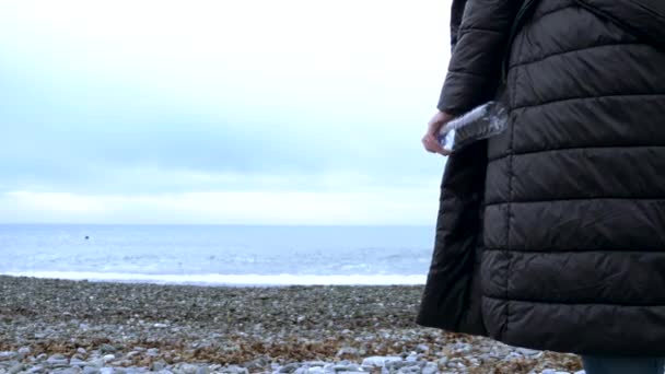 Nahaufnahme. Eine Frau wirft eine leere Plastikflasche an den Strand. — Stockvideo