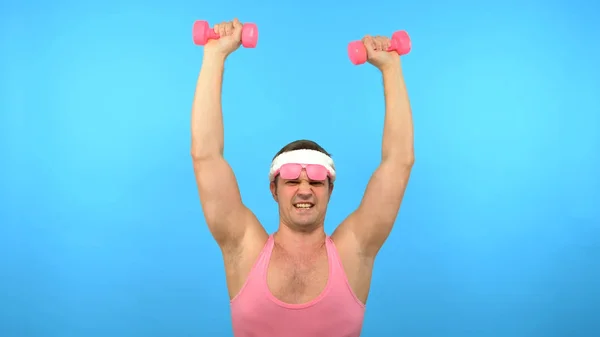 Homem bonito brincalhão em uma camisa rosa envolve-se na aptidão com halteres rosa. Fitness Brilhante. Acessórios de moda esportiva — Fotografia de Stock