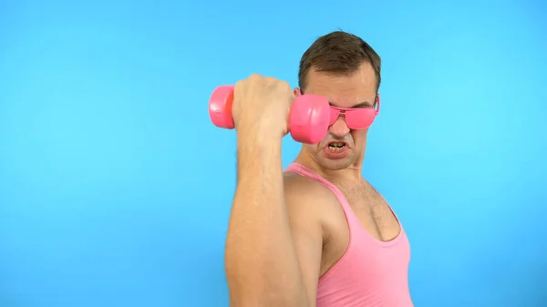 Homem bonito brincalhão em uma camisa rosa envolve-se na aptidão com halteres rosa. Fitness Brilhante. Acessórios de moda esportiva — Fotografia de Stock