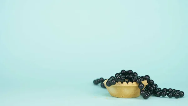 Seni fashion. minimalisme. manik-manik hitam jatuh ke dalam tartlet. latar belakang biru — Stok Foto