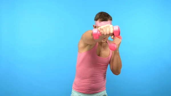 Juguetón hombre guapo en una camisa rosa se dedica a la aptitud con mancuernas de color rosa. Bright Fitness. Accesorios de moda deportiva — Foto de Stock
