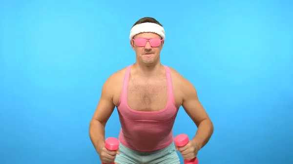 Juguetón hombre guapo en una camisa rosa se dedica a la aptitud con mancuernas de color rosa. Bright Fitness. Accesorios de moda deportiva —  Fotos de Stock