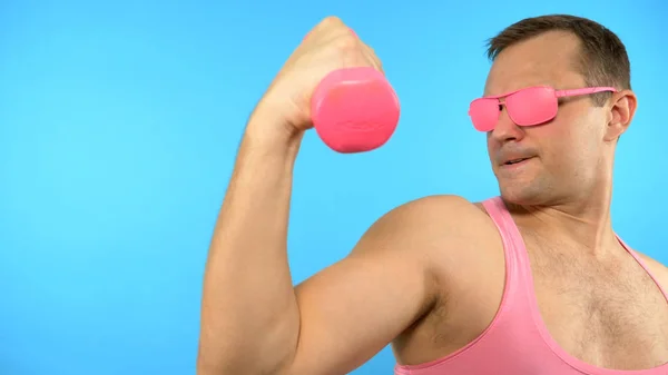 Playful handsome man in a pink shirt is engaged in fitness with pink dumbbells. Bright Fitness. Sports Fashion Accessories — 스톡 사진