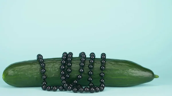 Fashion art food design. Fresh cucumber with a string of pearls. blue background — Stock Photo, Image