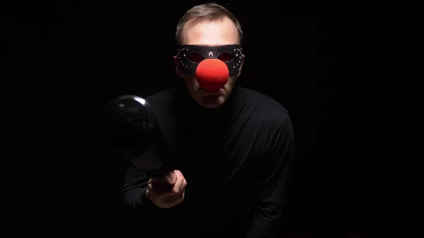 Man in een lederen masker met een rode clown neus zwaaien met een knuppel op een zwarte achtergrond — Stockfoto